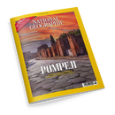 Schräg fotografiertes Magazin „National Geographic“ mit gelbem Rand und dem Titel „POMPEJI“, Ausgabe „AUGUST 2026“. Das Cover zeigt eine antike Ruinenstraße mit Ziegelmauern, Säulen und Zypressen unter rot-orangefarbenem Himmel; lesbare Texte: „LEBEN UND STERBEN IM SCHATTEN DES VESUV“ und „WIE FORSCHER DIE EREIGNISSE EINES HISTORISCHEN DRAMAS REKONSTRUIEREN“.