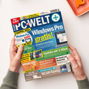 Schräg auf einem weißen Tisch liegende, farbig bedruckte PCWELT-plus-Zeitschrift, von zwei Händen einer nicht erkennbaren Person gehalten. Sichtbare Texte: „Windows Pro gratis!“, „Update mit 1-Klick“, „32 Seiten Extra“, „WLAN-AN-Tuning“, „Diese Downloads sind gefährlich!“ sowie „Ihr Recht auf Reparatur“; oben rechts liegt ein orangefarbenes Objekt.