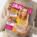Eine weibliche Person im beigefarbenen Strickpullover hält ein schräg fotografiertes, pink-gelbes Magazin mit dem Titel „plus für mich“. Auf dem Cover sind eine blonde Frau im gelben Oberteil, ein Gericht sowie die Texte „Das beruhigt den Magen“, „Glanz ins Haar“, „Gesunde, schöne Haut“, „Luxus-Camping in Dänemark“, „Einmal im Leben…“ und „Ist Hautkrebs bald heilbar?“ zu erkennen.