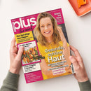 Schräg gehaltenes Magazin „plus magazin – plus für mich“ mit zwei Händen vor weißem Hintergrund; auf dem Cover eine blonde weibliche Person im gelben Oberteil. Sichtbare Texte: „Gesunde, schöne Haut“, „Glanz ins Haar“, „Das beruhigt den Magen“, „Neue Impfungen & Medikamente“, „Luxus-Camping in Dänemark“ und „Einmal im Leben …“. Oben rechts liegt ein orangefarbenes Objekt.