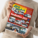 Eine Person im hellbeigen Strickpullover hält ein schräg fotografiertes, rot-gelb gestaltetes Magazin mit dem Titel „promobil“ und der Überschrift „Neuheiten 2021“. Das Cover zeigt mehrere weiße und graue Wohnmobile sowie Texte wie „Über 50 Camping- und Stellplätze“, „Ratgeber & Zubehör“ und „Lithium-Akkus im Test“.