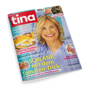 Schräg fotografiertes Cover der Zeitschrift „tina“ mit rotem Logo, einer lächelnden blonden Frau in hellblauer Bluse und türkisfarbenem Hintergrund. Sichtbare Texte: „Kopfschmerzen einfach wegdrücken“, „Cremige Kuchen ohne Backen“, „SCHLANK mit dem Tomaten-Trick“, „Die schönsten Camping-Trends“, „Lifting mit Rouge“ und „Jetzt wird’s fröhlich-bunt“; außerdem Bilder von Kuchen, Gnocchi, Campingbus und Kleidung.
