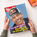 Schräg gehaltene Zeitschrift mit blau-rotem Cover, auf dem ein lächelnder Mann in dunklem Anzug und schwarz-grauer Kappe mit „Red Bull“-Logo abgebildet ist. Sichtbare Titelzeilen lauten „Lars Klingbeil“ und „Macht er so die SPD wieder fit?“; zwei Hände in grauen Strickärmeln halten das Papier vor weißem Hintergrund.