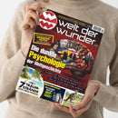 Schräg gehaltenes Magazin „welt der wunder“ in den Händen einer Person mit beigem Strickpullover; rot-schwarzes Cover mit weißem Logo, gelber Zeile „ENTDECKEN–STAUNEN–WISSEN“ und Bildcollage aus Porträts, Figuren und Landschaft. Sichtbare Überschriften: „Enthüllt: aus den KRANKEN-AKTEN der Mächtigen“, „Die dunkle Psychologie der Weltgeschichte“, „7 TRAUM-STRÄNDE“ und „Wie erkennt man ein DEEP-FAKE?“.