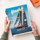 Zeitschrift „Yacht“ mit Titelbild eines schwarzen Regattasegelboots mit farbigen Segeln auf blauem Wasser vor hellblauem Himmel. Das Heft wird von zwei Händen mit grauen Strickärmeln gehalten; sichtbare Titelzeilen sind „Ostsee-Perlen“, „Bordstrom“ und „Boris Neue“.